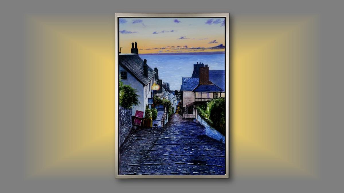 Handgemaltes Ölbild Küstendorf in Abendstimmung auf Leinwand, gepflasterte Gasse mit Blick aufs Meer, mit silbernem Rahmen – Beispiel im Raum