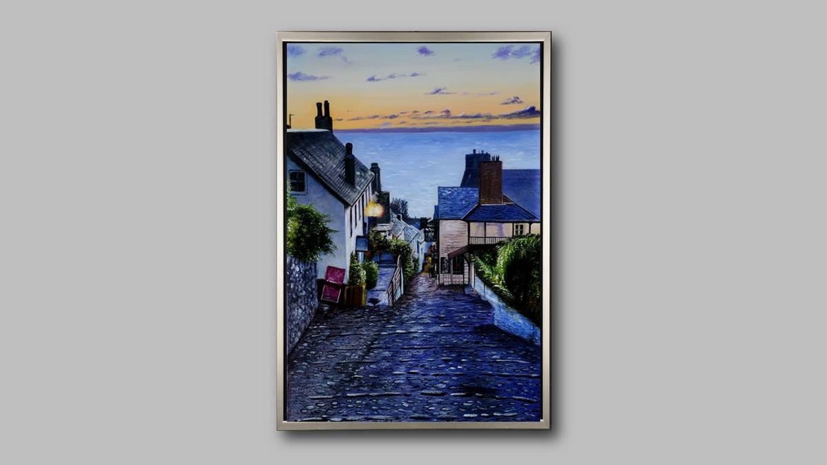 Handgemaltes Ölbild Küstendorf in Abendstimmung auf Leinwand, gepflasterte Gasse mit Blick aufs Meer, mit silbernem Rahmen – Beispiel im Raum