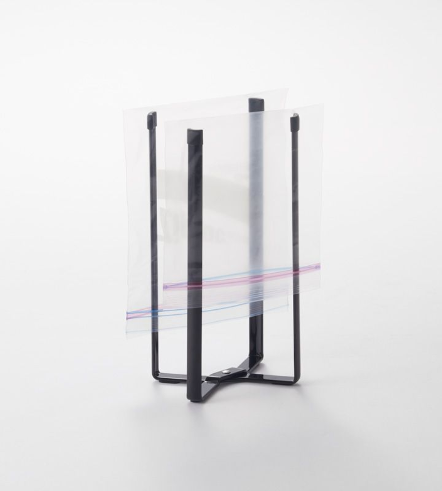 Der YAMAZAKI TOWER Mehrzweckständer Küche - Schwarz hält einen offenen Zip-Top-Beutel aufrecht, um ihn leicht befüllen zu können. Er ist auf einer schlichten weißen Fläche abgebildet.