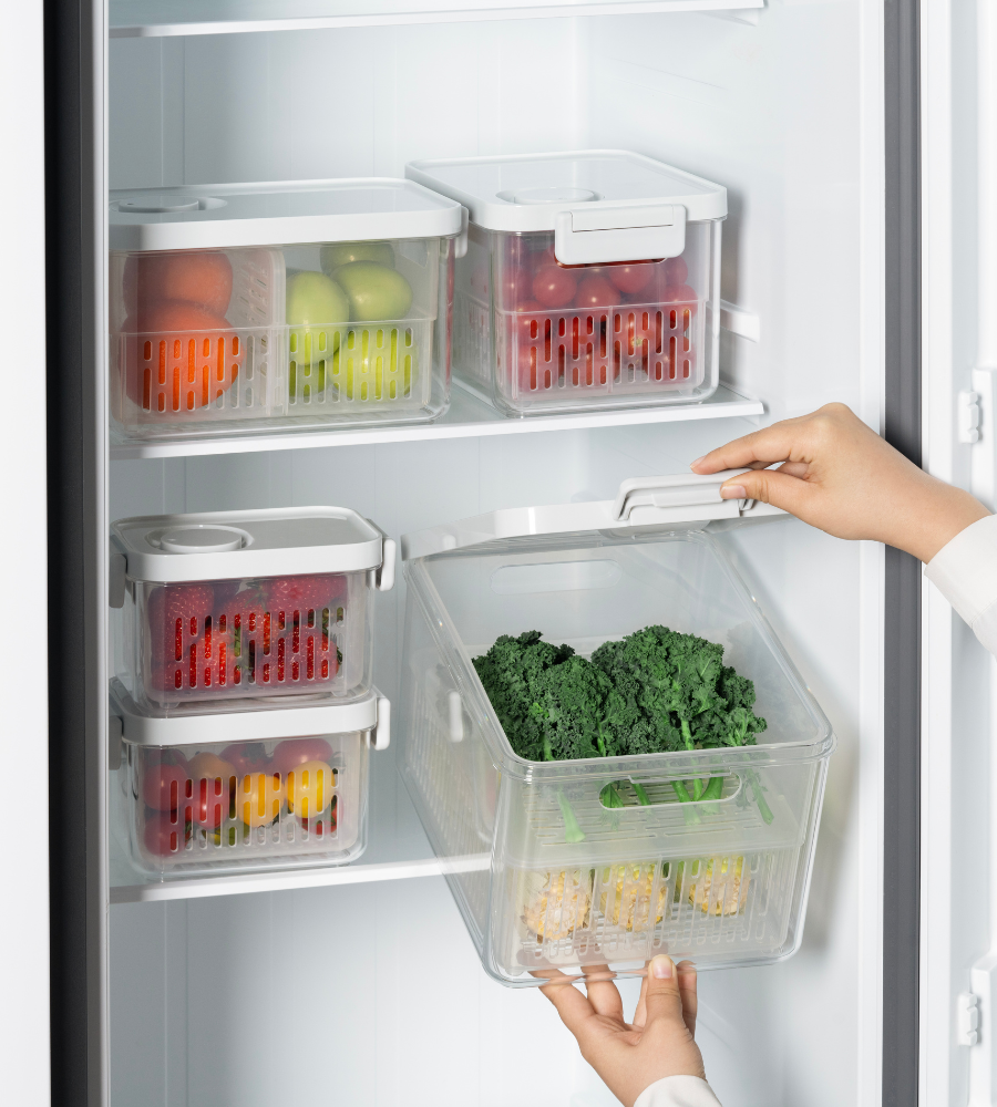 Una persona tiene le verdure a foglia verde in un contenitore trasparente DATEMATE KLAR Bianco con timer di conservazione di BNB x VCN nel frigo. Grazie al loro design impilabile, questi contenitori simili tengono in ordine frutta e verdura sullo scaffale.