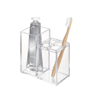 Der iDesign CLARITY - Kosmetik Organizer KLAR II, ein klarer Acrylhalter, bewahrt eine Zahnpastatube und eine Bambuszahnbürste mit weißen Borsten übersichtlich auf - eine ideale Bad Aufbewahrungslösung auf einem schlichten weißen Hintergrund.